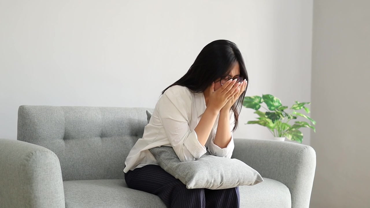 年輕女子坐在家中沙發上，臉上流露出焦慮、恐慌、困惑和壓力的表情。
