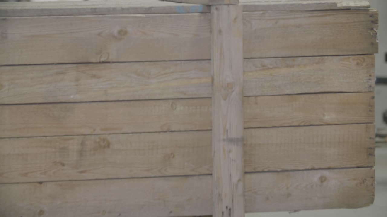 una carretilla elevadora que transporta una gran caja de madera se mueve hacia la cámara en una nave industrial