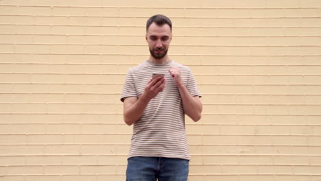 young excited man overjoyed looking at the phone and celebrating success outdoors