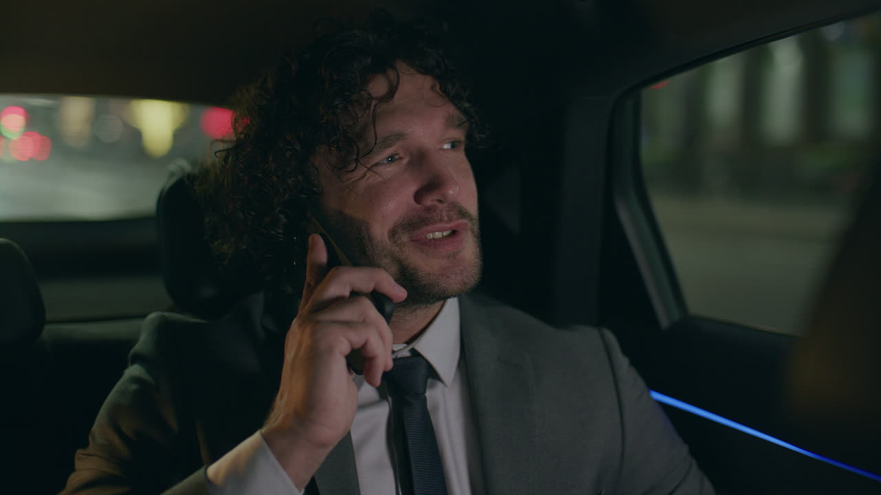 Young Businessman Smiling while Speaking on Phone in Car at Night