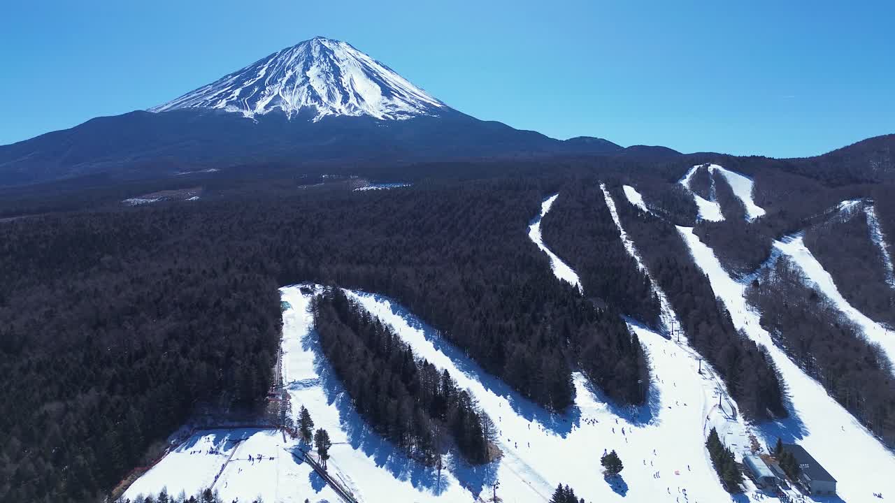 Veduta aerea con drone di un paesaggio sciistico e di un resort sulla neve, con piste ghiacciate e percorsi di neve fresca, circondato da boschi e dalla cima del Monte Fuji a Narusawa, Giappone, un'immagine di turismo e natura asiatica.
