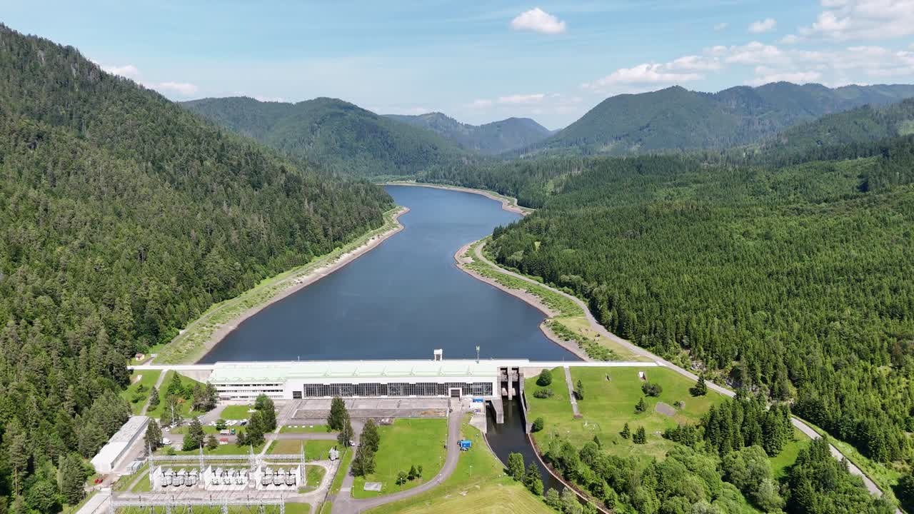 Aerial view of Čierny Váh hydroelectric dam surrounded by dense forests and mountain landscape on a sunny summer day in Slovakia