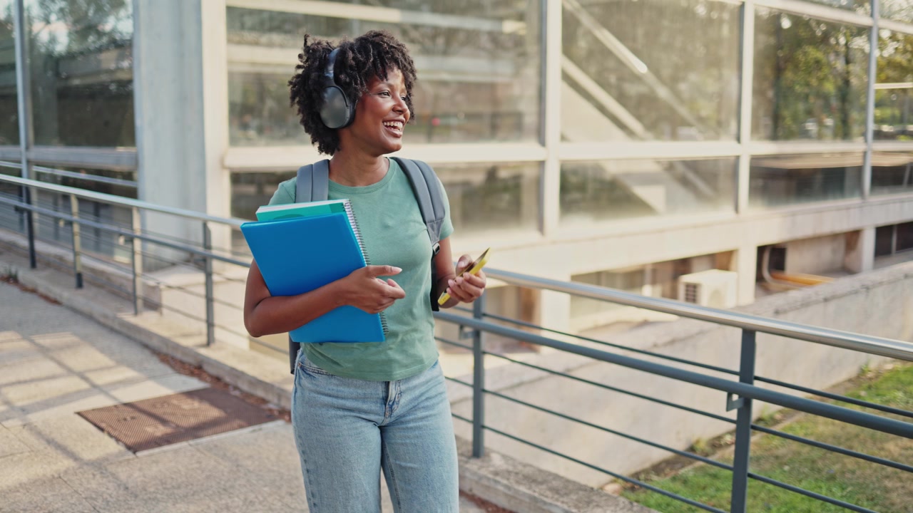 Étudiante afro-américaine heureuse marchant et utilisant son téléphone sur le campus