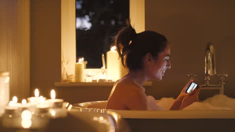 woman relaxing in a bubble bath with a mobile phone