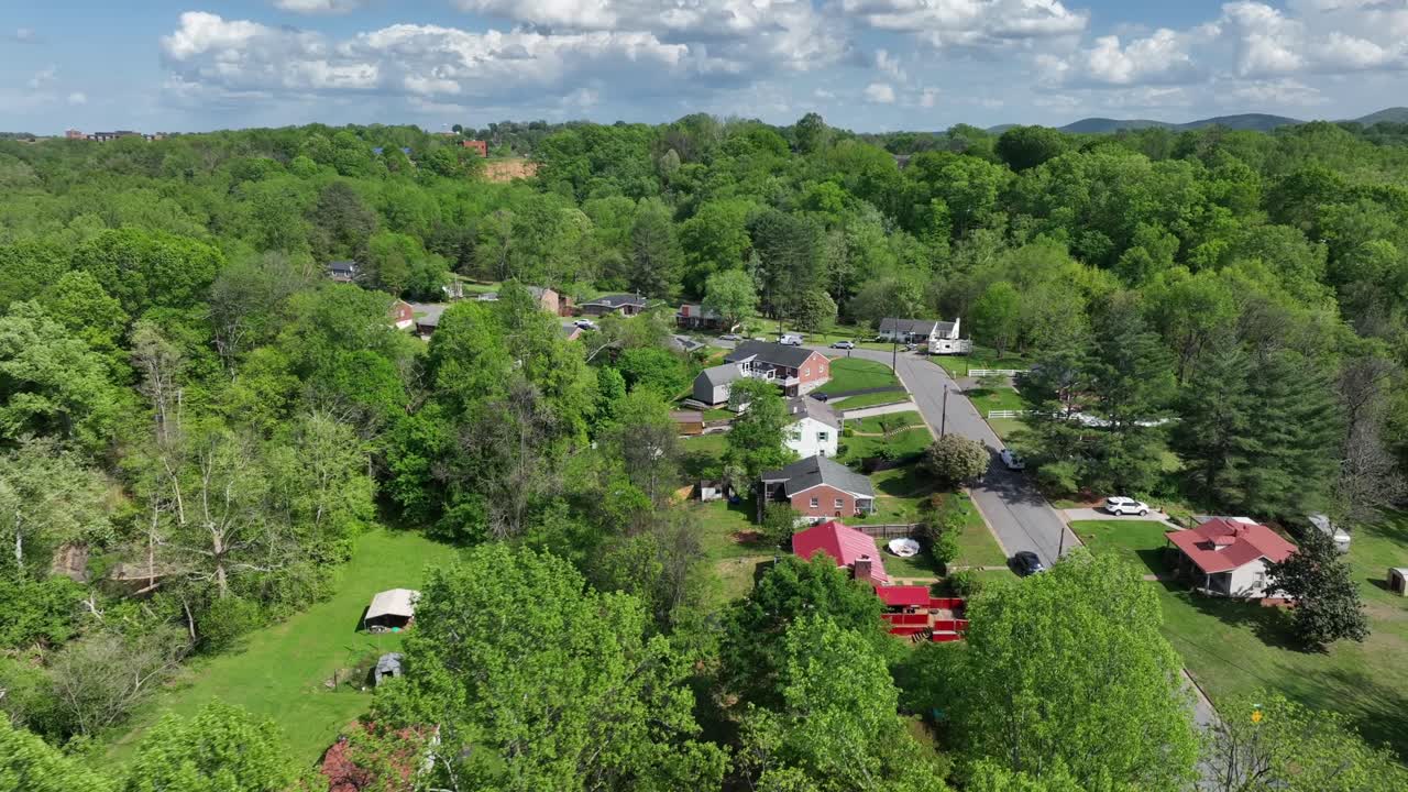Colored houses in green forest landscape during sunny day. Homes in suburb of America town. Clouds at sky. Aerial approaching shot.