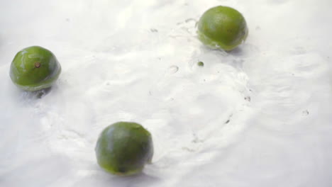 slomo of limes falling into water on white backdrop