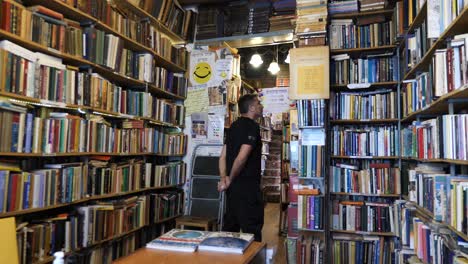 Customer-in-cozy-secondhand-bookshop-looking-at-the-books,-bookstore-interior