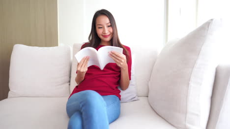 Mujer-Asiática-Está-Cómodamente-Sentada-En-El-Sofá-Y-Leyendo-Un-Diario-De-Libros-Con-Tapa-Blanca