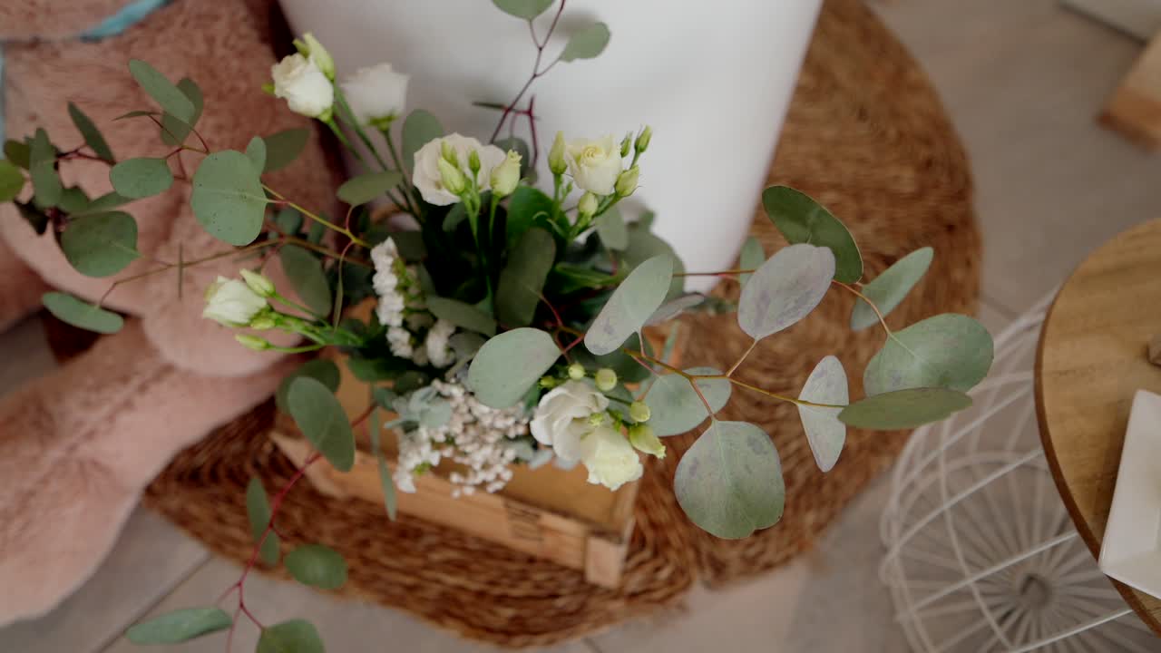 White roses and eucalyptus arranged in rustic wooden box indoor setting