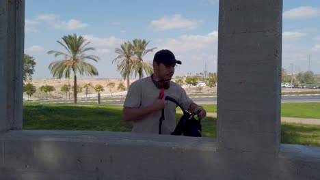 young man with backpack, cap and headphones around his neck in a park.