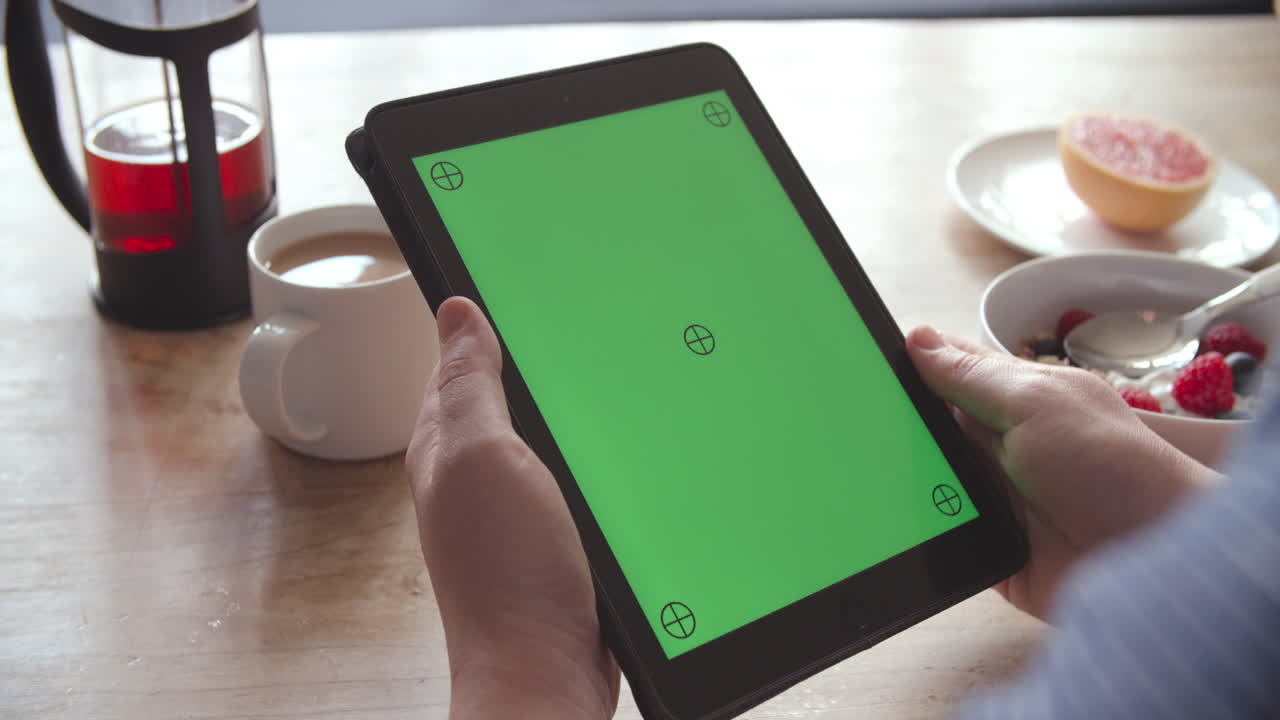 manos sosteniendo una tableta digital con pantalla verde en el desayuno