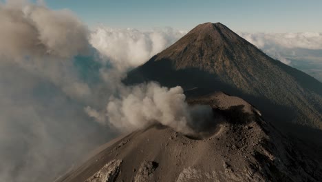 Der-Vulkan-Fuego-Spuckt-Vulkanasche-Und-Smog-Aus,-In-Der-Ferne-Der-Vulkan-Agua-In-Guatemala