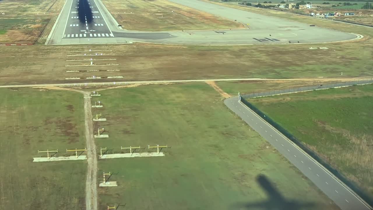 An immersive cockpit view of the shadow of a jet airplane on the ground approaching to the runway for landing, as seen by the pilot from cockpit. Hazy summer morning at early hour.