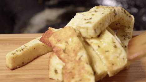 Fried-herb-cheese-stacked-on-wooden-board,-defocused-pan-in-background