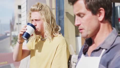 Two-Caucasian-male-surfboard-makers-sitting-on-a-bench-and-drinking-takeaway-coffee