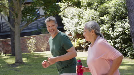 una feliz pareja de ancianos diversos corriendo y sosteniendo una botella de agua al aire libre soleado