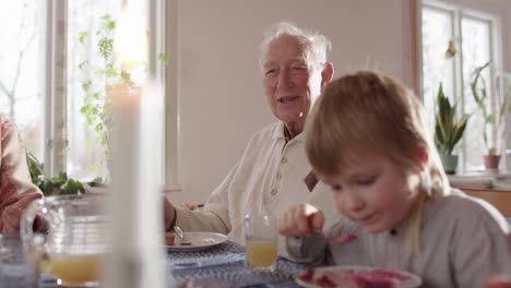 young boy eats cake next to great-grandfather telling a story at dining table