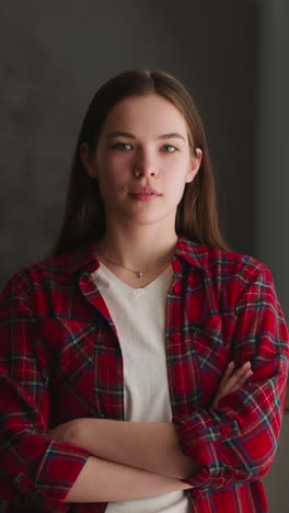 pretty smiling teenage girl with crossed arms in checkered shirt stands near window at home slow motion. domestic lifestyle and casual apparel style