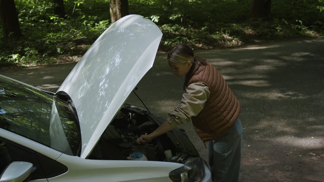 Woman examining engine with open hood of vehicle on side of road