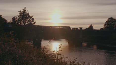 Static-shot-of-a-tram-crossing-the-bridge-over-River-Forth-at-golden-hour-in-Stirling,-UK