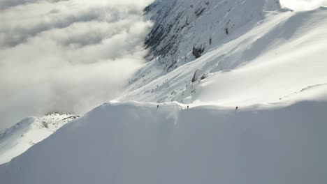 Snow-covered-Piatra-Craiului-Mountains-with-hikers-in-distance,-surrounded-by-clouds,-conveying-a-sense-of-adventure