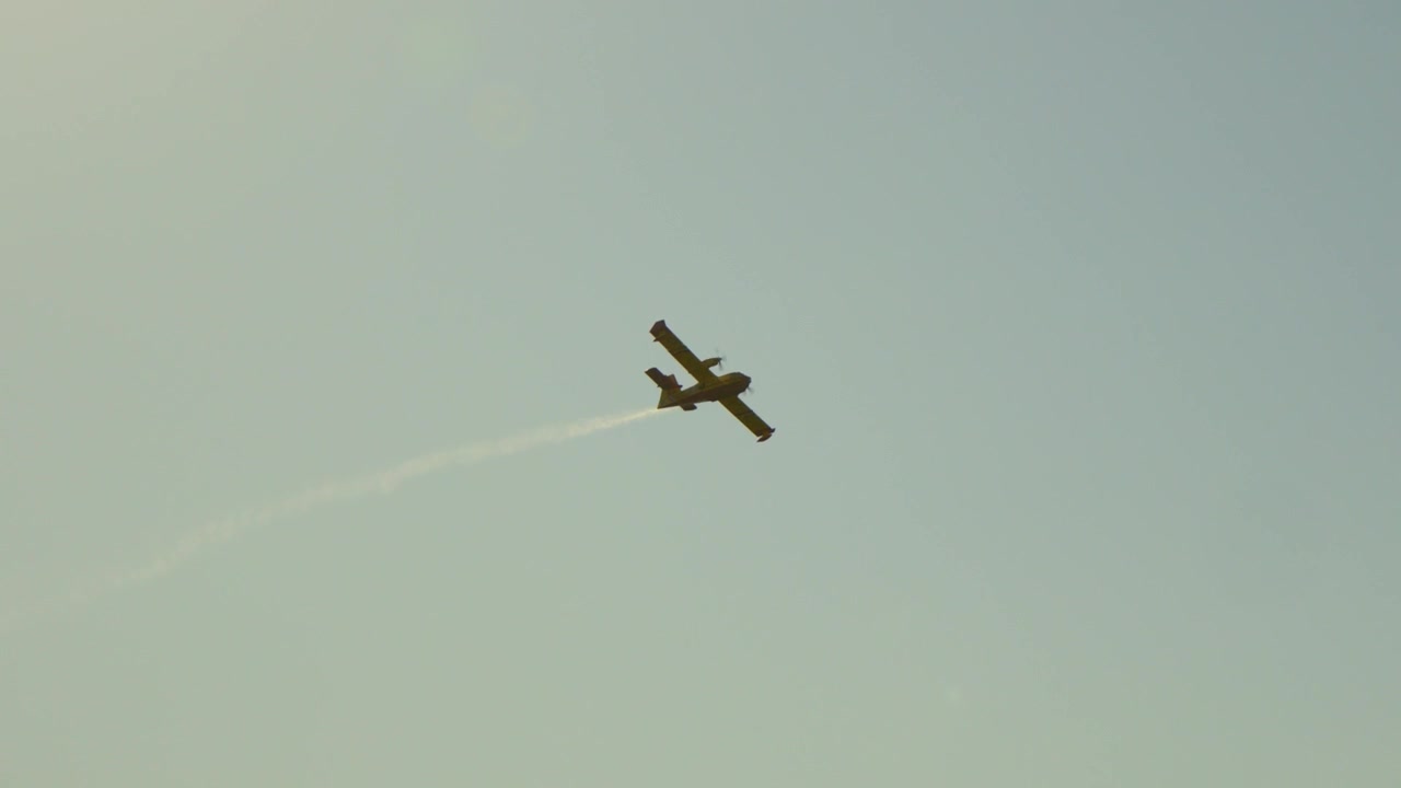 Håndholdt sporing fra lav vinkel av et Canadair brannfly med røyksky på himmelen.