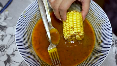 corn cob being dipped in spice sauce inside bowl