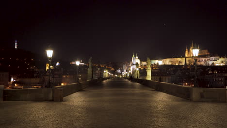 Una-Magnífica-Vista-De-La-Calzada-Pavimentada-Del-Puente-De-Carlos-En-El-Centro-Histórico-De-Praga,-Chequia,-Por-La-Noche,-Sin-Gente,-Estatuas-Y-Linternas-A-Ambos-Lados,-El-Castillo-De-Praga-Al-Fondo