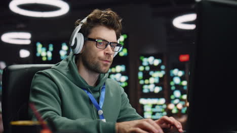 Headphones man coding computer in server room closeup. Developer listening music