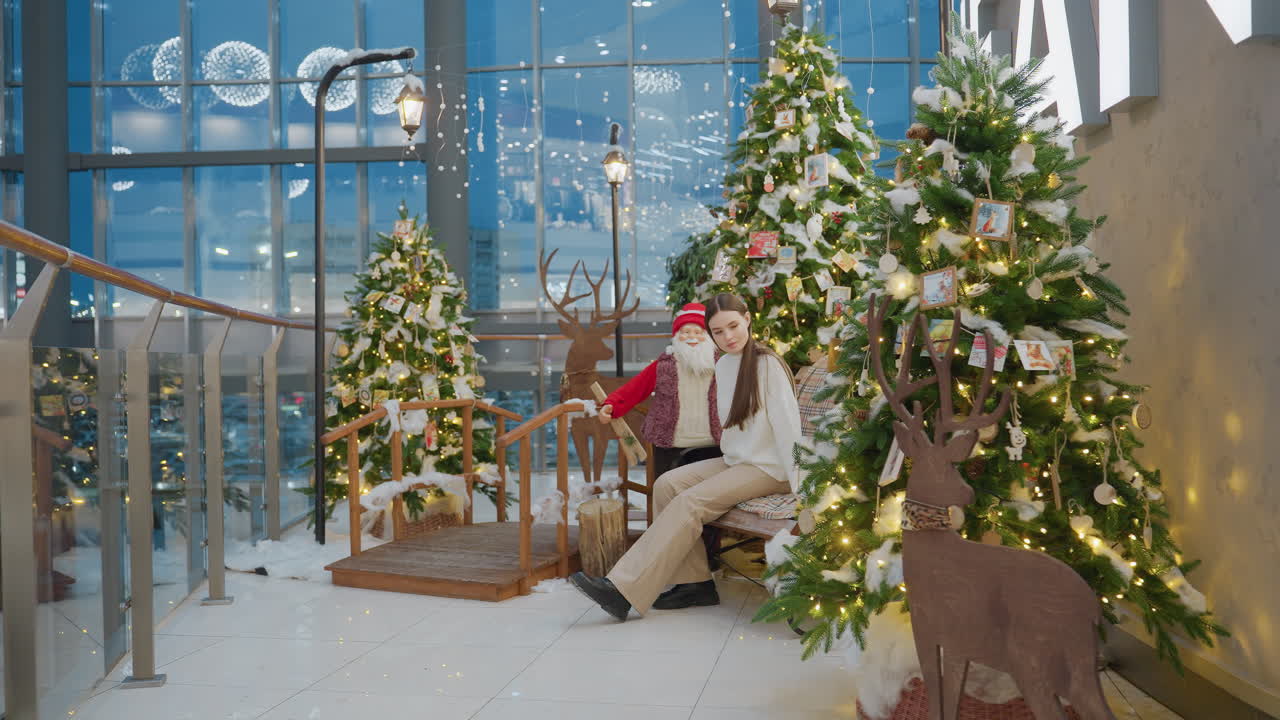 Lady walking up to decorative seats and stretching her leg forward in a Christmas-themed mall area, surrounded by festive trees, lights, and a wooden reindeer decoration