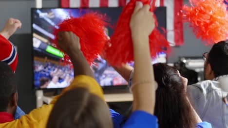 aficionados con pom-poms viendo el partido en casa