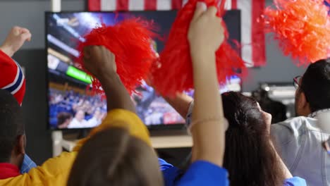 fans with pom-poms watching match at home