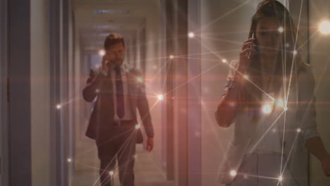 Colleagues walking down business corridor, using smartphones while network overlay glowing overhead