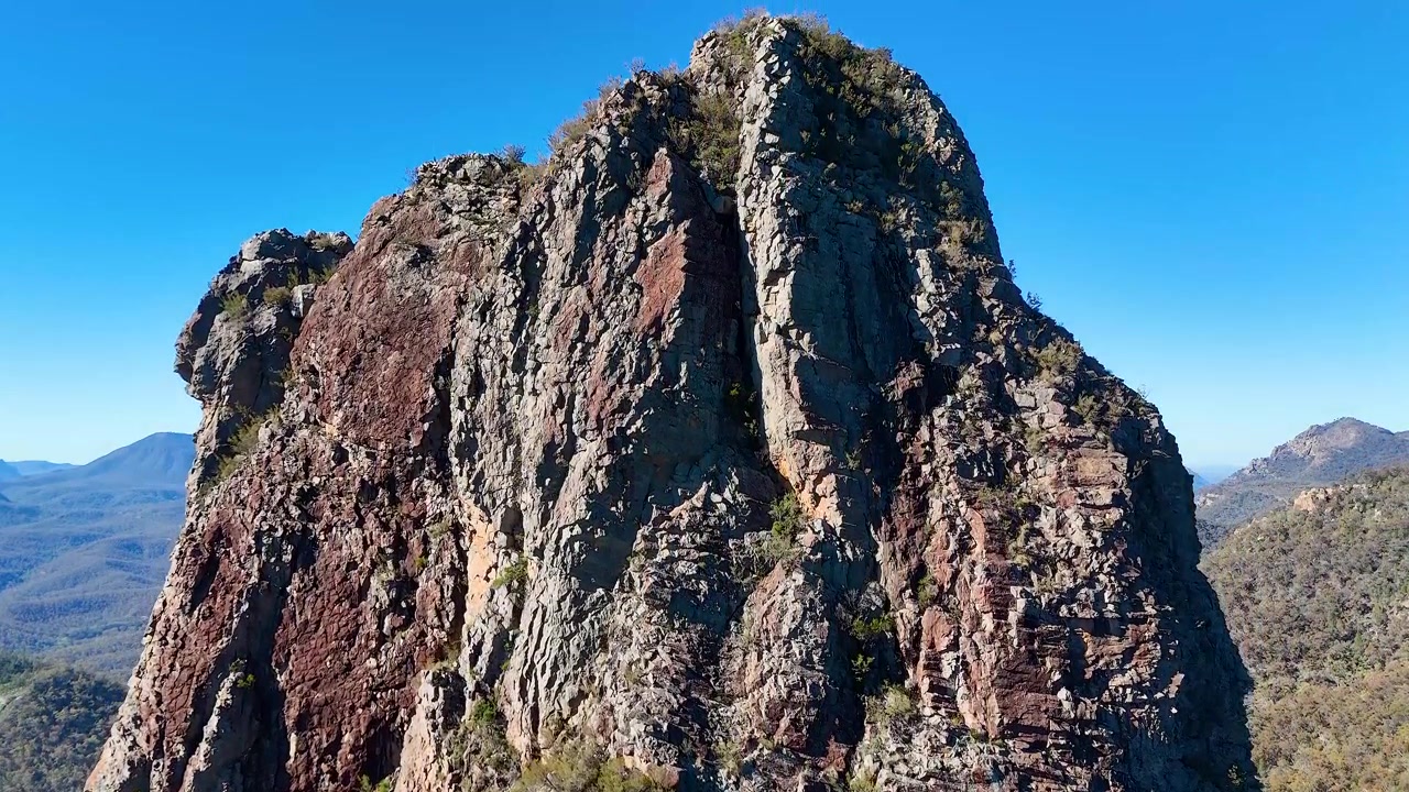 Toma de dron de picos volcánicos escarpados bajo un cielo azul claro en el Parque Nacional Warrumbungle, Australia