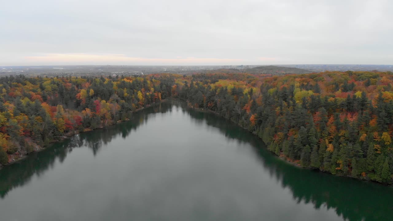 imágenes aéreas sobre el lago rosa en gatineau hills quebec pasando desde por encima de la mitad del lago al estacionamiento sobre una bicicleta en un camino curvo