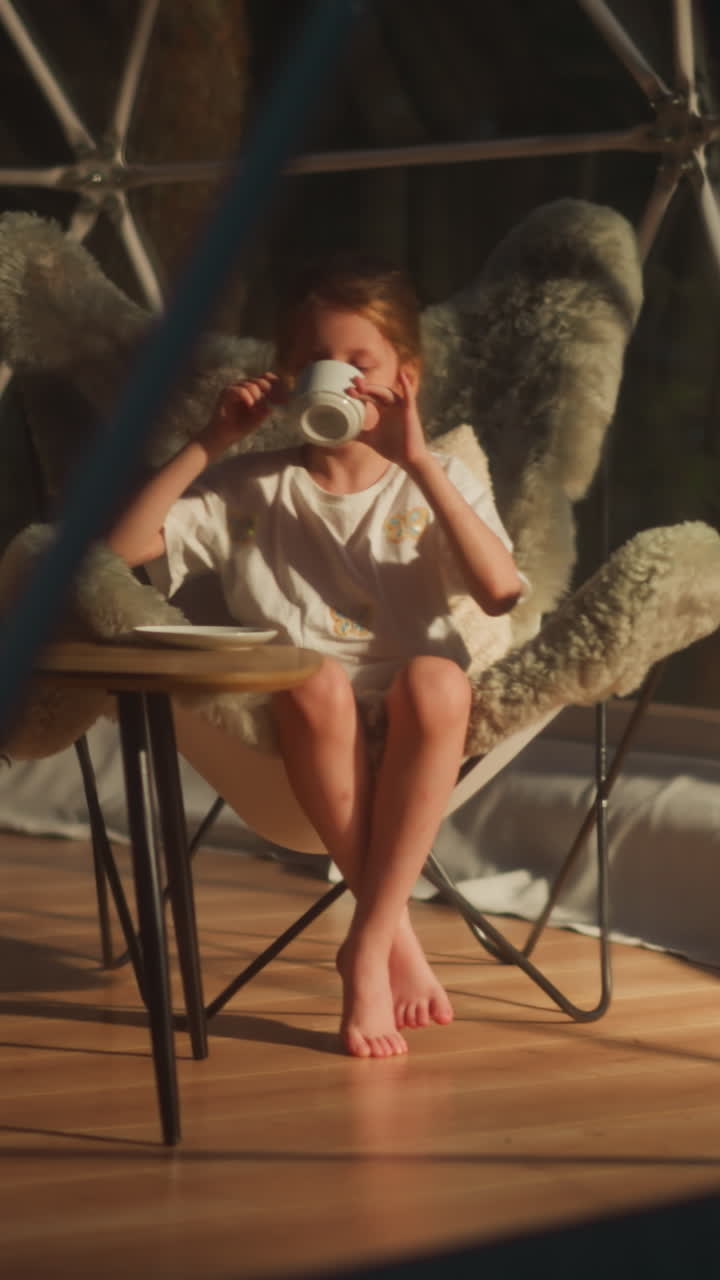 글램핑  에서 맛있는 음료를 마시는 아이들. 작은 소년은 음료를 고 소녀는 텐트에서 테이블에 앉아 컵을 마시고 캠프에서 저녁 차를 마시고 있습니다.