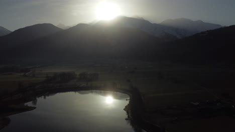 Flying-over-a-lake-with-the-reflect-of-the-sun-shinning-over-the-Mont-Blanc,-early-in-a-winter-morning