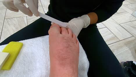 professional pedicurist shapes and smooths the toes on a man's right foot using an emery board