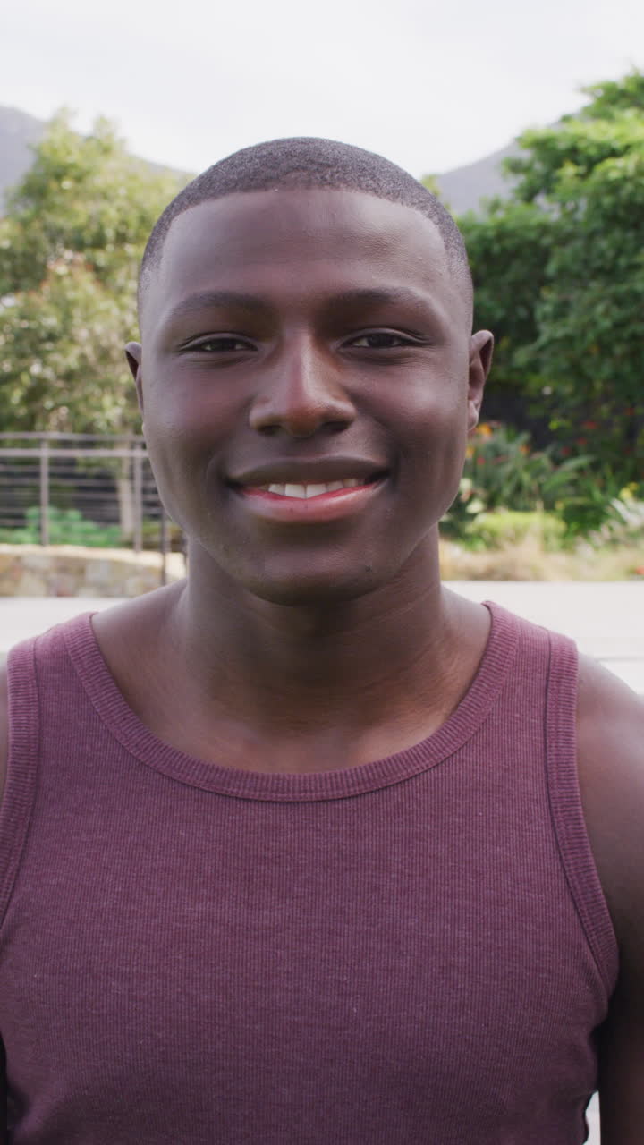 retrato de video vertical de un hombre afroamericano sonriendo a la cámara al aire libre en el jardín
