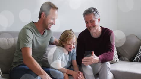 Animation-of-bokeh-over-happy-grandfather,-father-and-son-on-sofa