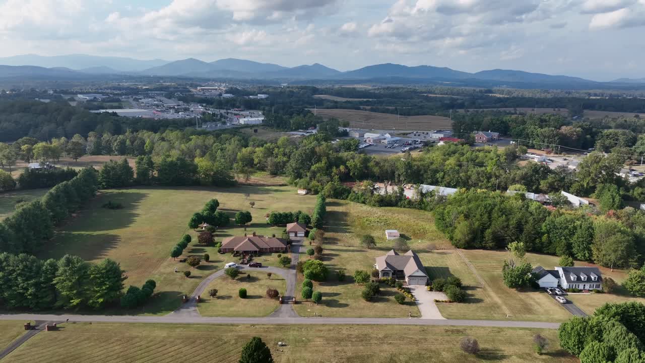 Drone view of American countryside with scattered houses, open fields and distant blue mountains under cloudy sky. Rural lifestyle and wide landscapes in Virginia, USA. Aerial wide shot