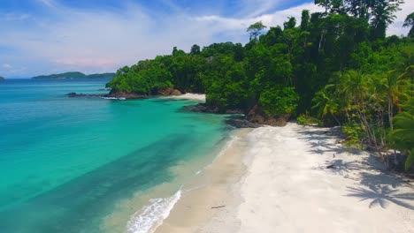 Forward-Aerial-Flight-Across-White-Sand-Beach-Edge-with-Palm-Trees-and-Coral-Rocky-Island