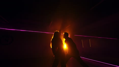 contemporary romantic dance in the dark studio. male and female dancers performing at the backdrop of yellow light projector. low angle view.