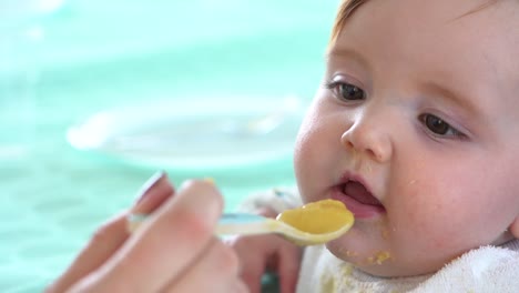 a mother's hand carrying a spoon full of baby food is twirled around just before it enters into the toddlers mouth, close up shot slow motion