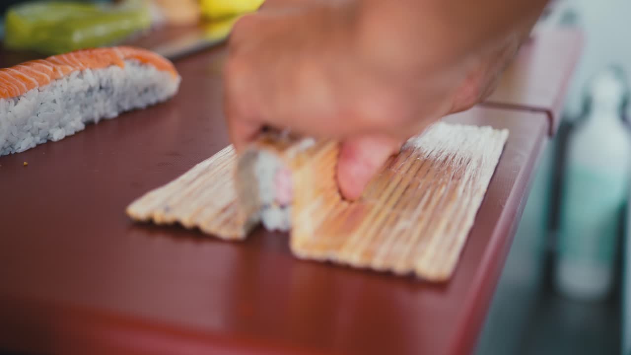 un chef profesional presiona un rollo de arroz para hacerlo compacto, preparando un plato de sushi, cocina tradicional japonesa