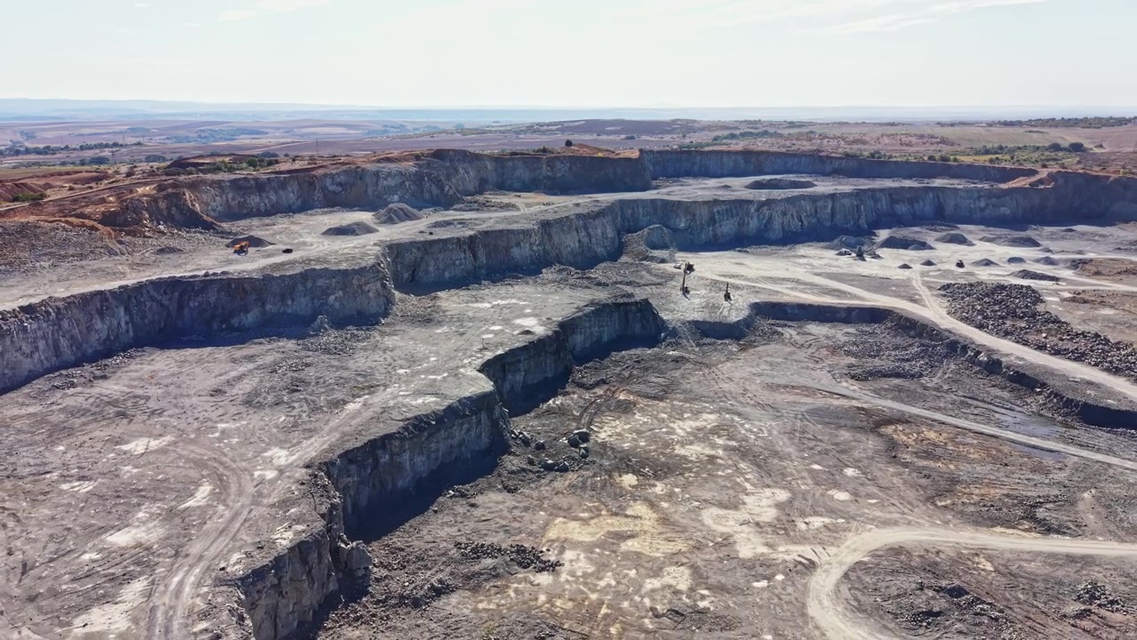 Workers are extracting granite from a large quarry during daylight in a vast open area surrounded by hills