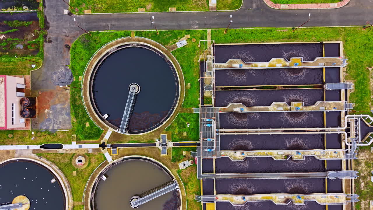 Water treatment facility located in a large industrial area with several circular and rectangular tanks for processing wastewater during daylight hours