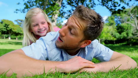 Padre-Tirado-En-El-Césped-Antes-De-Que-Su-Hija-Asome-La-Cabeza-Detrás-De-él