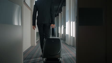 businessman with travel suitcase walking at hotel corridor. man arriving hotel