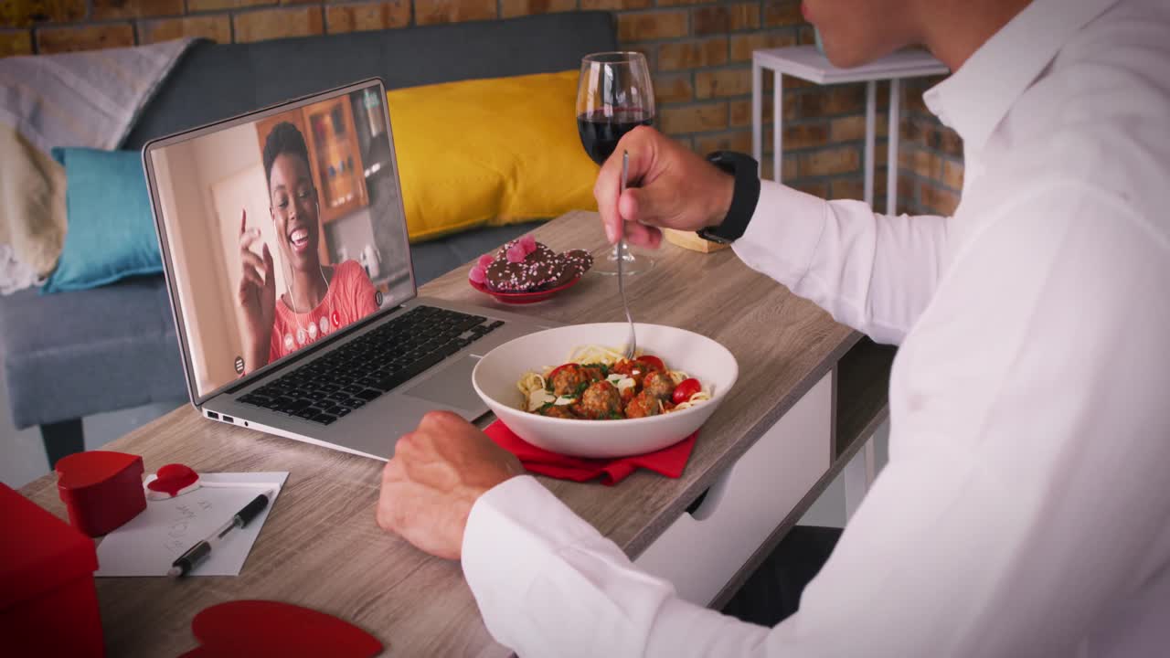 pareja diversa en una cita de san valentín videollamada mujer en la pantalla de la computadora portátil saludando hombre comiendo comida